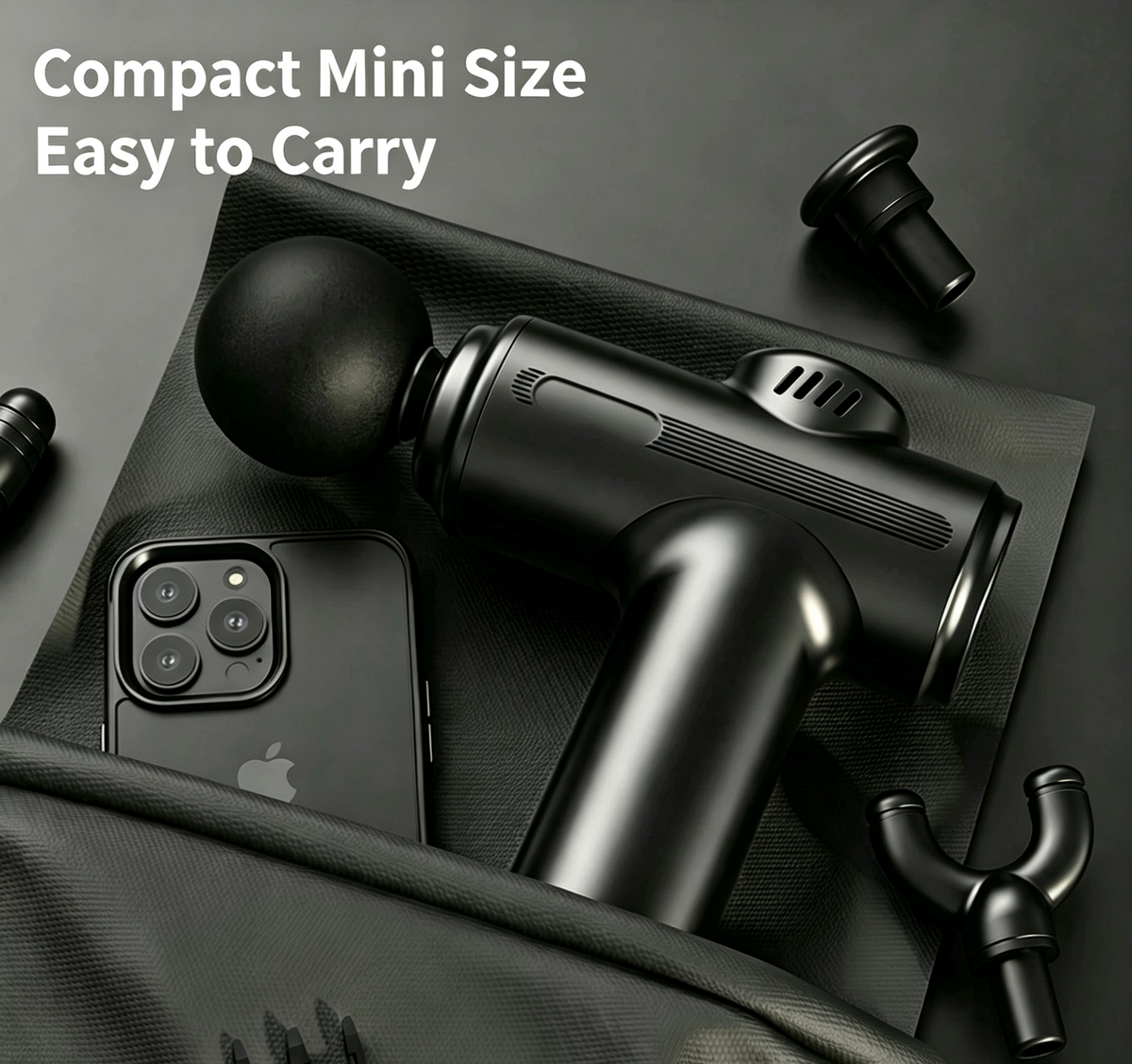 A compact black handheld massage gun shown on a dark textured surface with a smartphone beside it and several interchangeable heads around it. White text in the upper left reads 'Compact Mini Size Easy to Carry'.