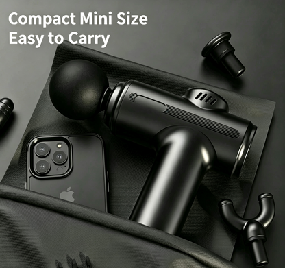 A compact black handheld massage gun shown on a dark textured surface with a smartphone beside it and several interchangeable heads around it. White text in the upper left reads 'Compact Mini Size Easy to Carry'.